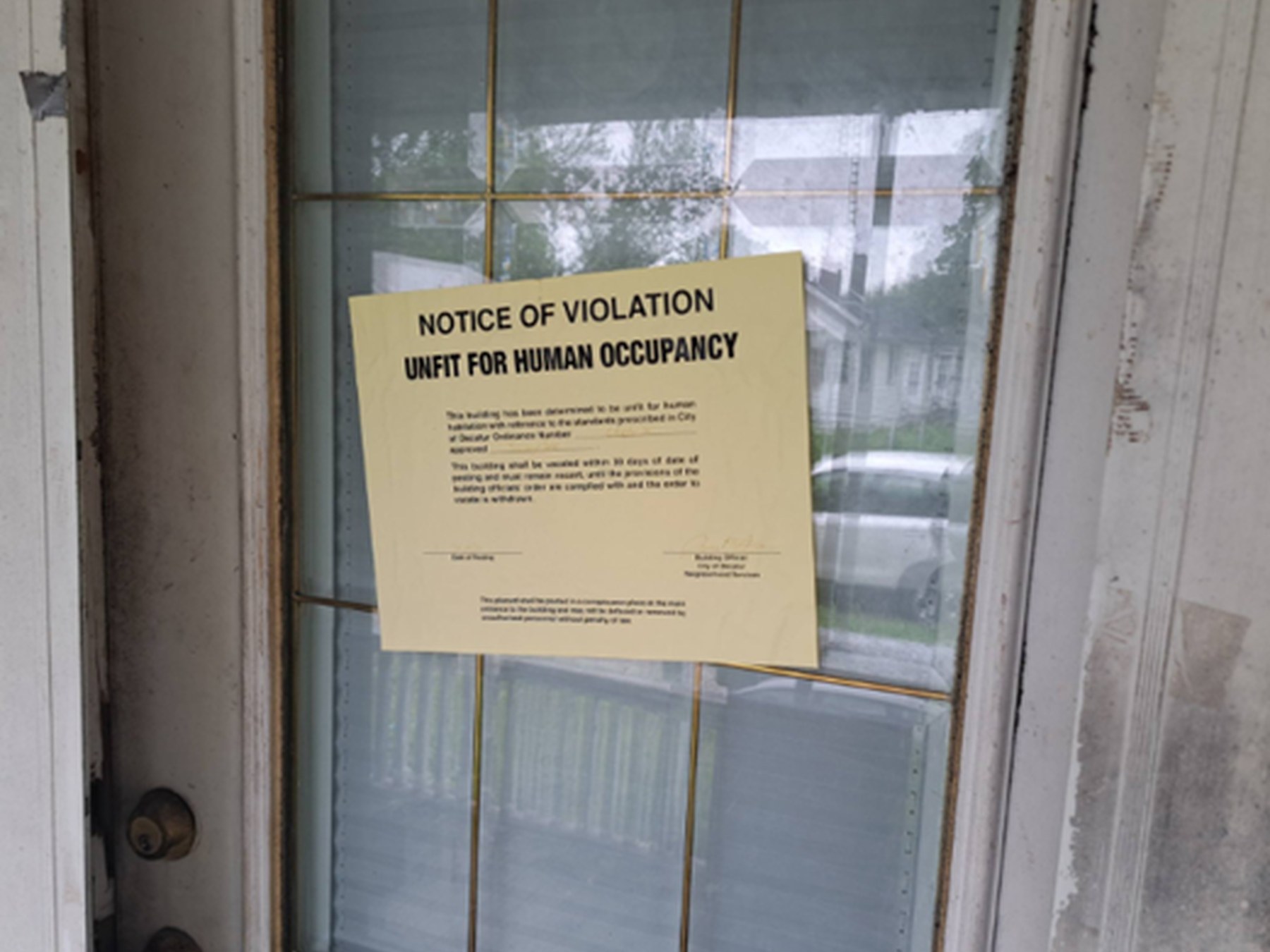 A city code enforcement notice of violation taped to the door of a run-down house, the kind of enforcement action that signals a pressured owner.