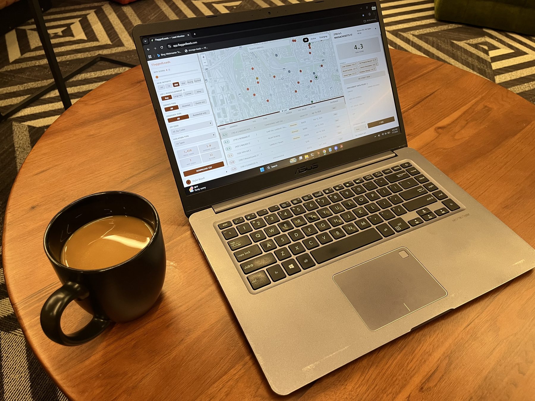 A laptop on a kitchen table showing the FlaggedLeads distress map and lead list over morning coffee. Reviewing code-violation leads from a desk instead of driving neighborhoods.